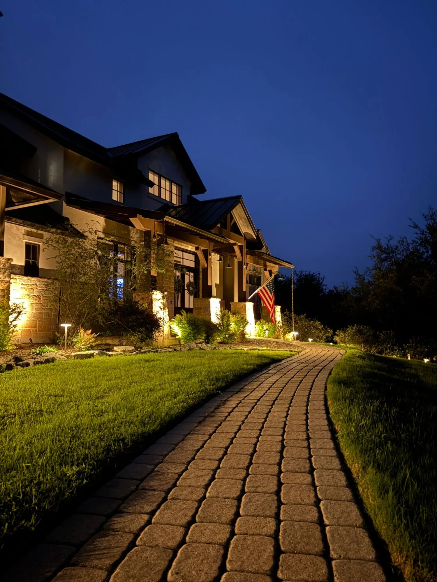 Stone columns and timber porch lit along a curving paver walkway lined with path lights