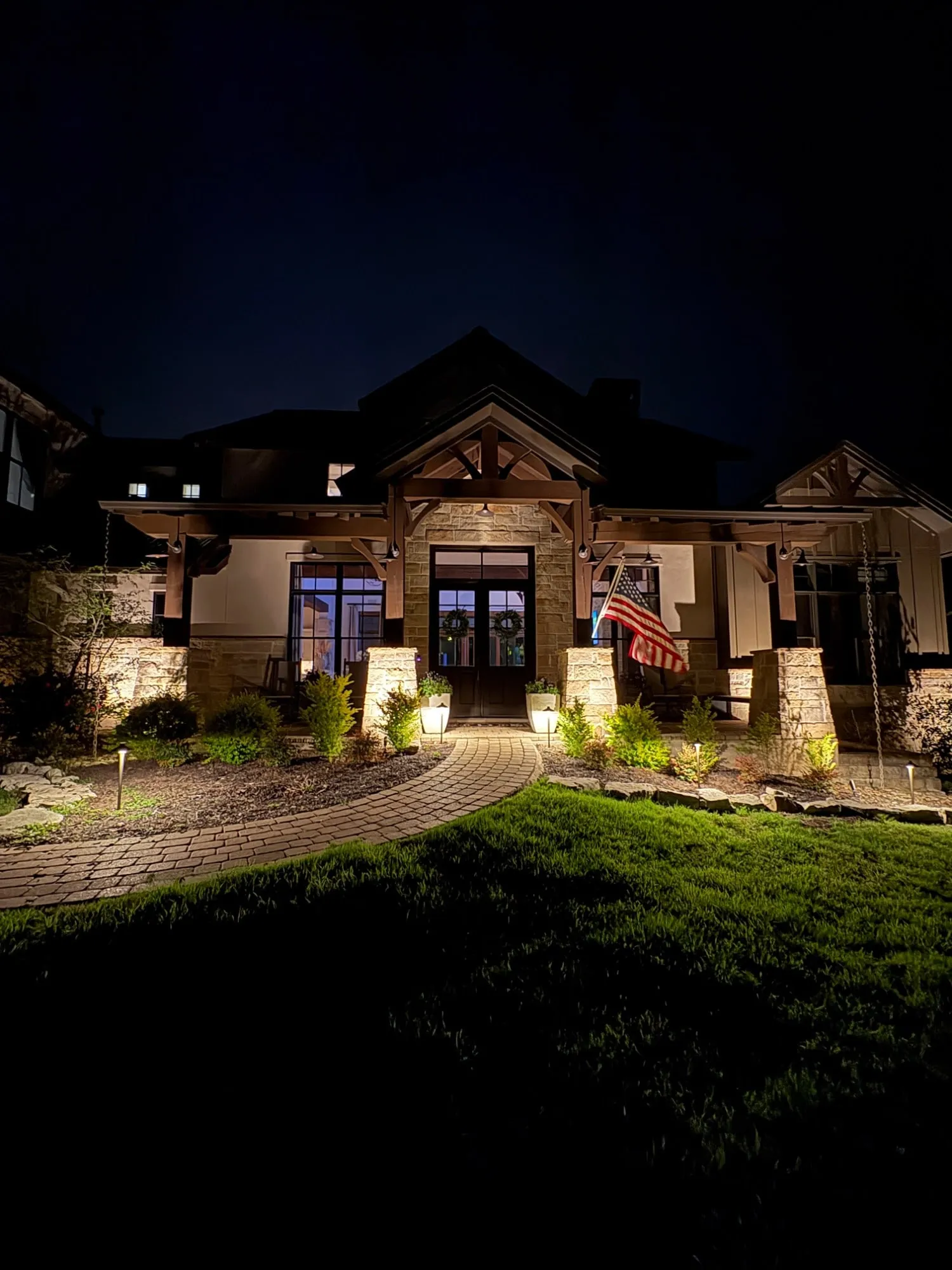 Covered front porch with uplit stone columns, lit planters, and path lights along a paver walkway