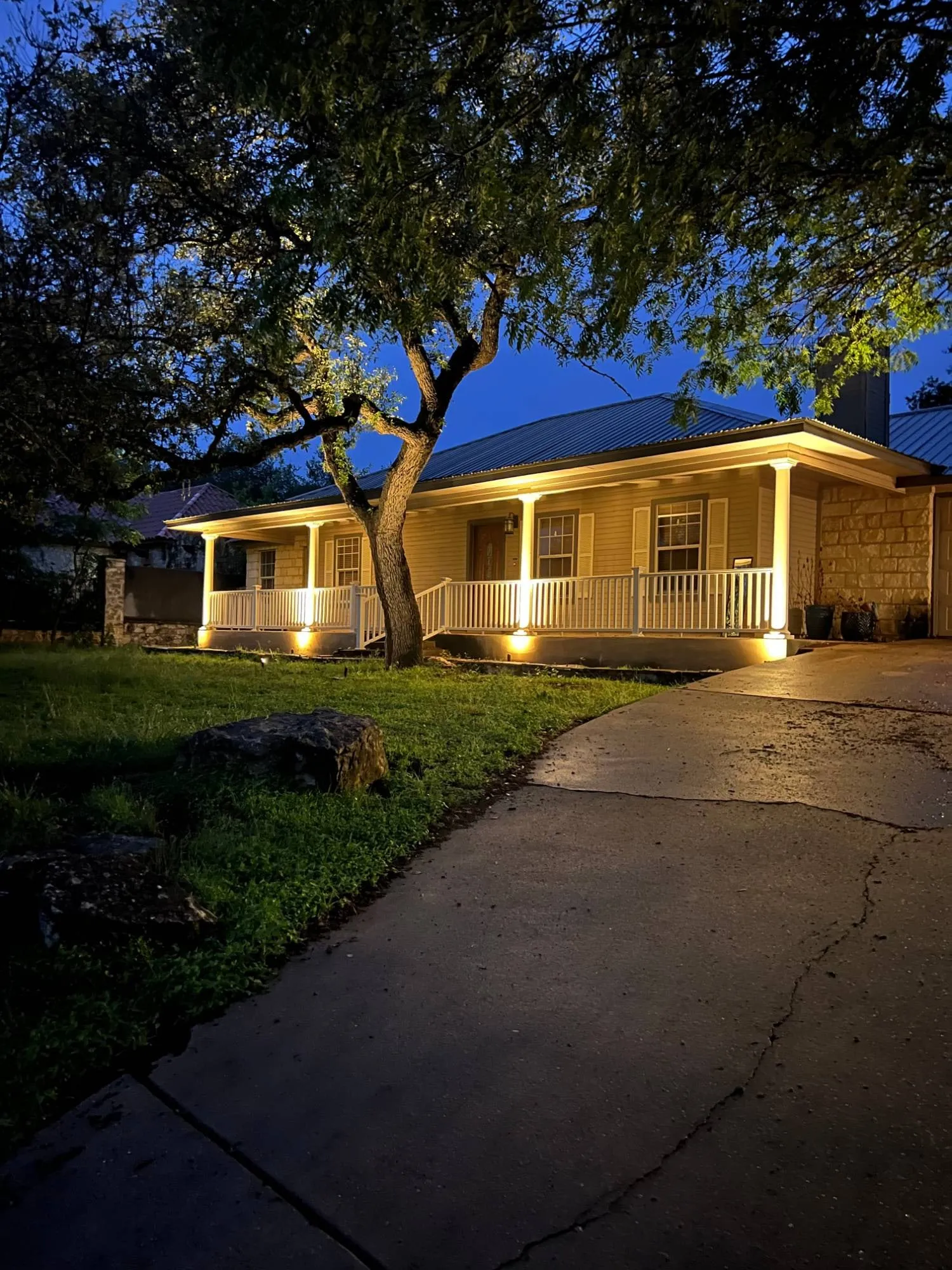 Covered front porch with each column uplit, a softly lit ceiling, and an uplit tree in the front yard