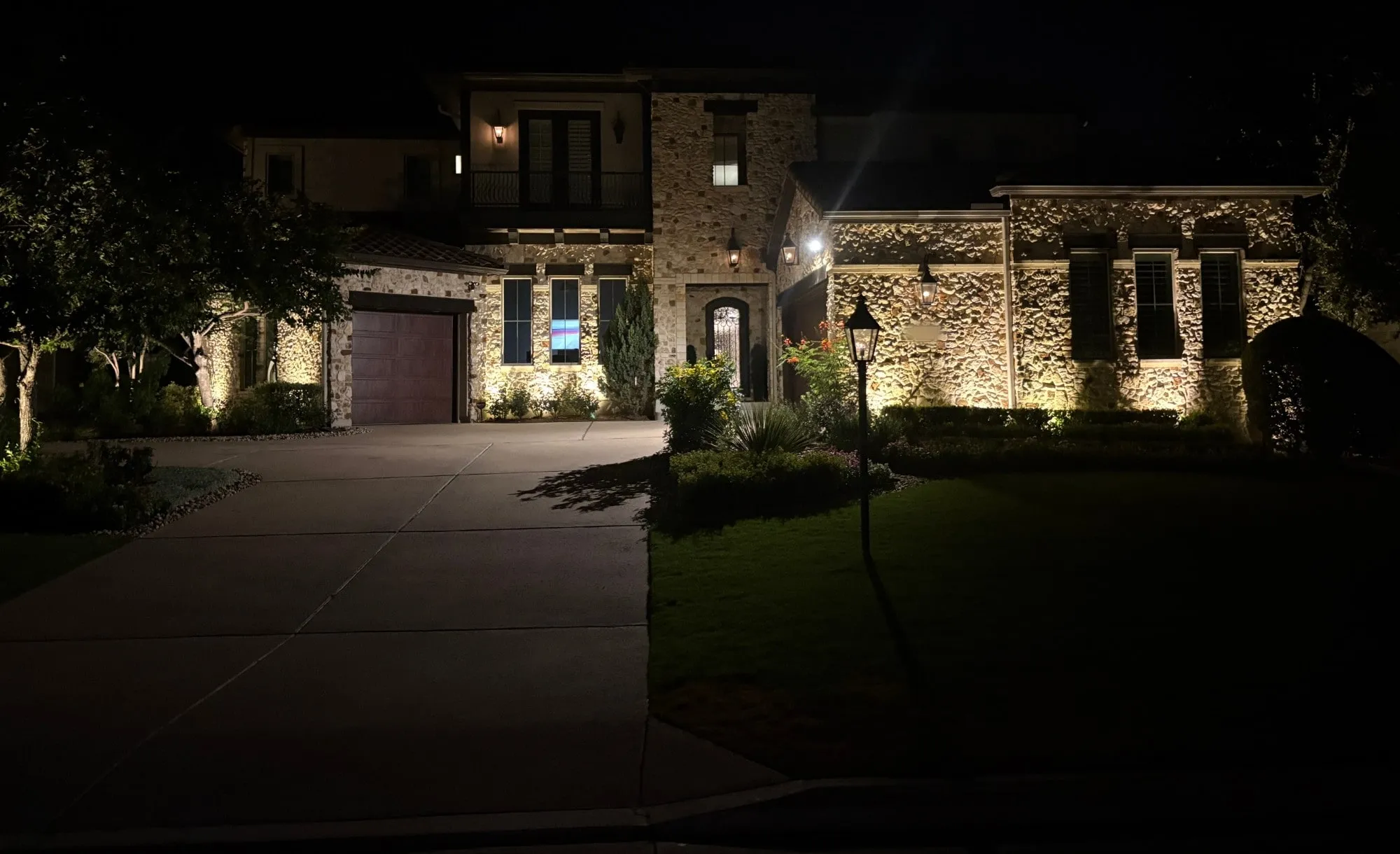 Two-story stone estate with light grazing across the entire facade, columns, and entry