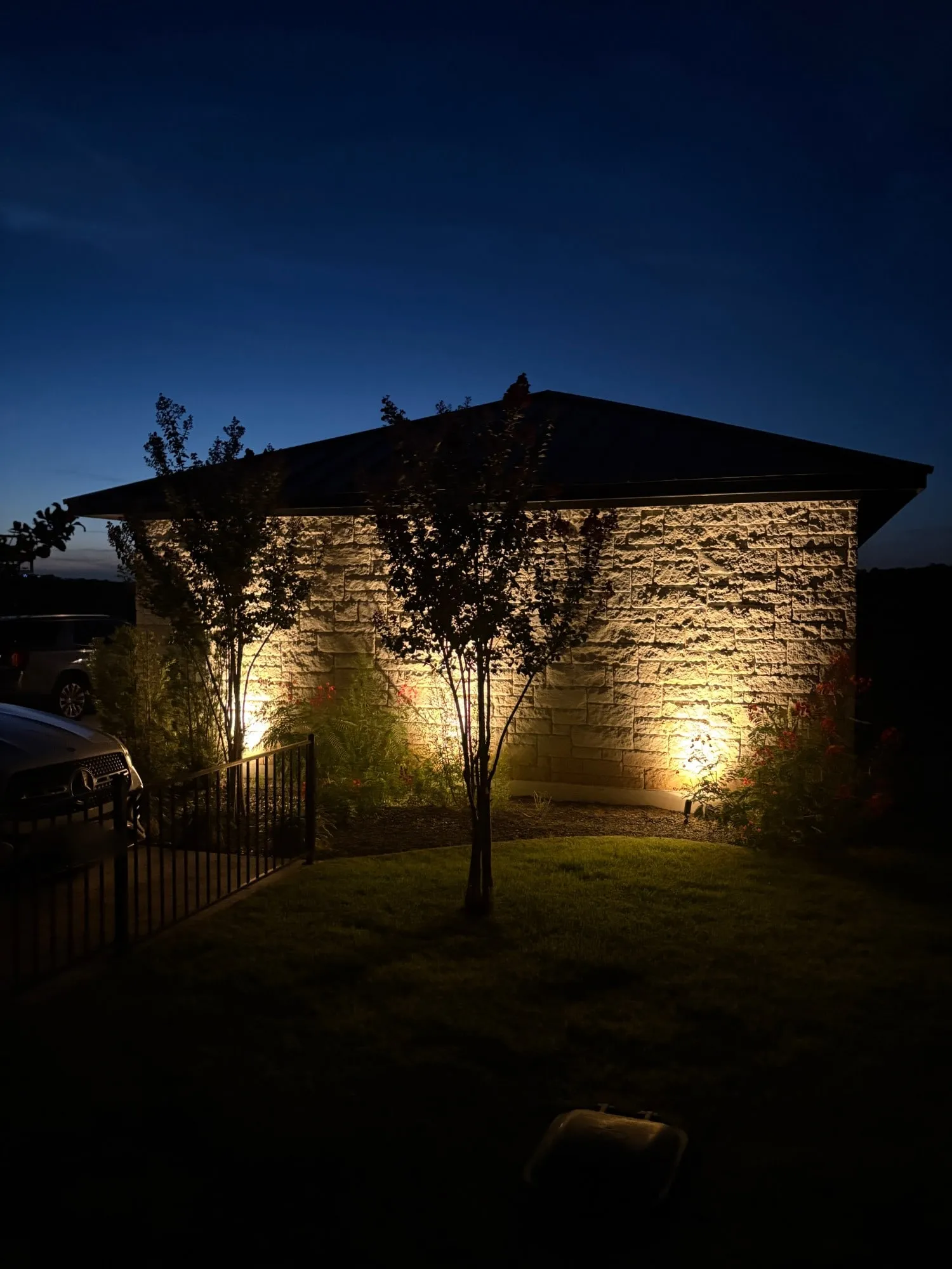 Stone garage wall washed with warm light behind crepe myrtles and red blooms