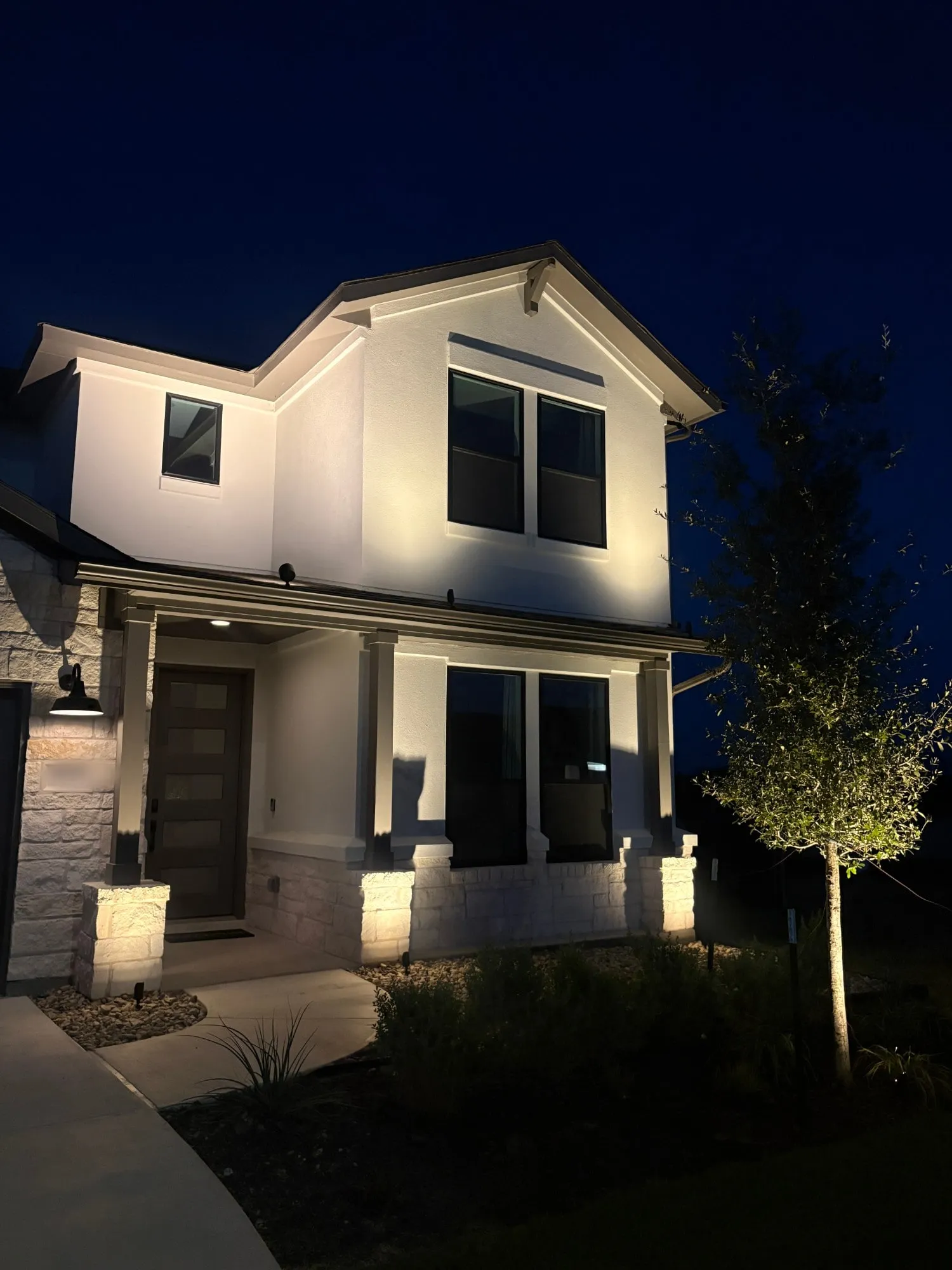 White stucco two-story home with uplit stone columns and gable