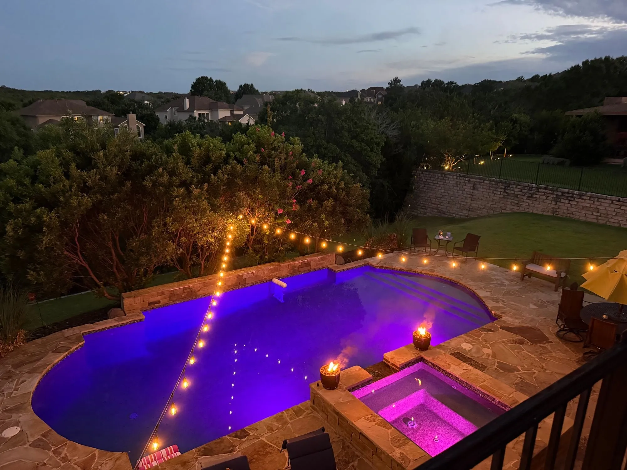 Café string lights strung across a backyard pool and flagstone deck at dusk