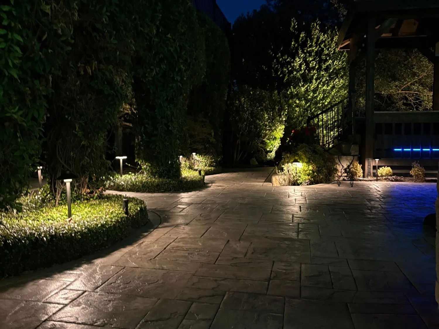 Stamped stone patio and garden path lined with path lights, with uplit shrubs and a lit gazebo