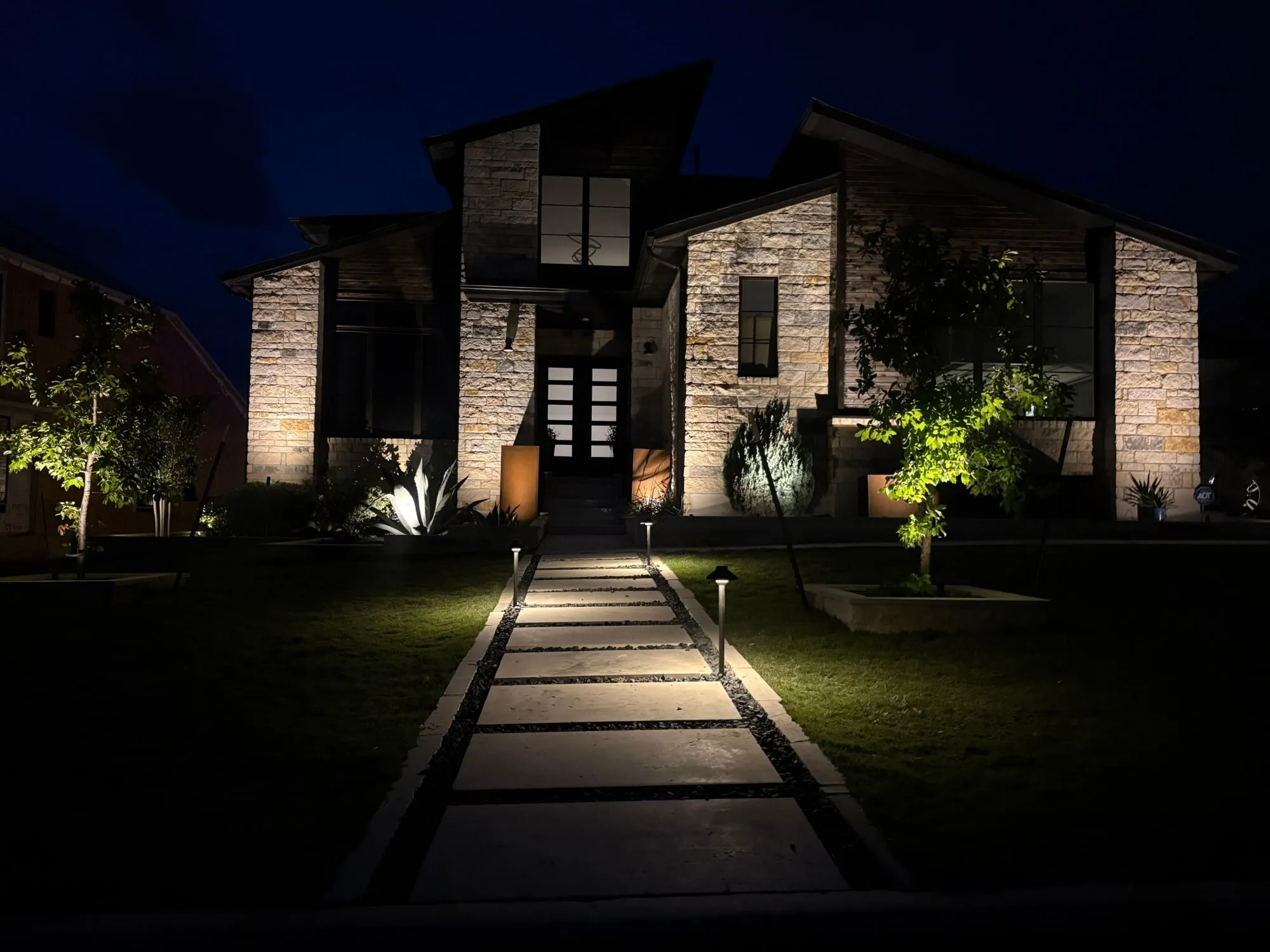 Stepping-stone walkway lined with path lights leading to a modern stone home