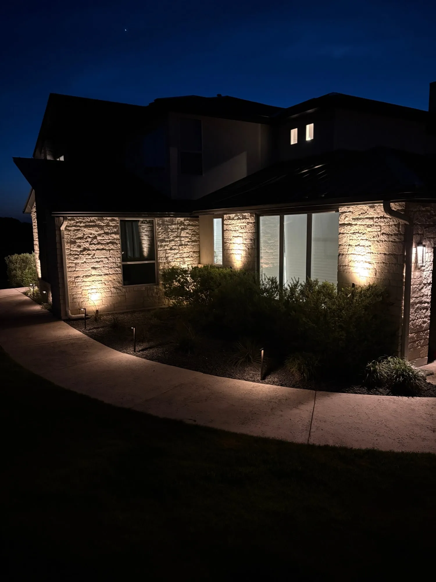 Walkway and stone wall lit along the side of a home